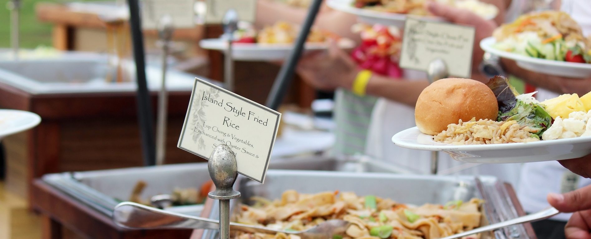 Outdoor Hawaiian buffet with people serving traditional island food.