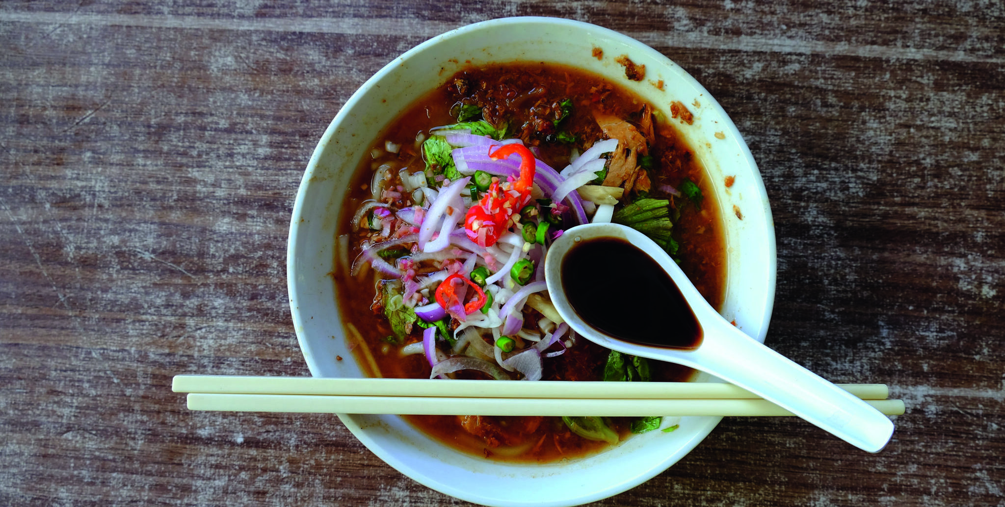 Asam laksa with chilli, red onion and a spoon and chopsticks.