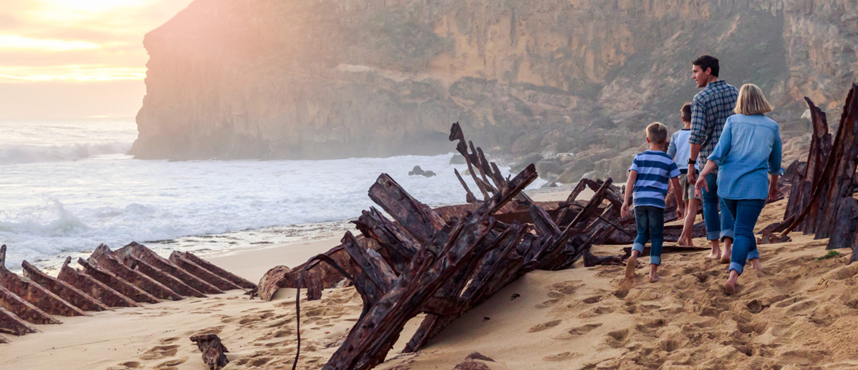 Family walking along beach next to shipwreck. Waves crashing in the background.