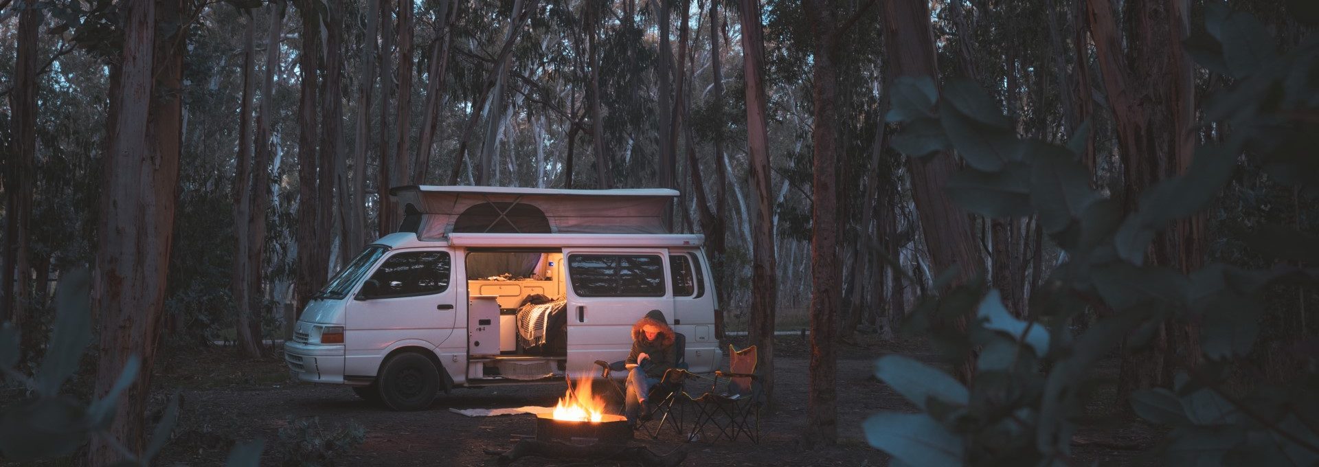 A van parked in Kuitpo Forest at night, with a woman sitting beside a bonfire.